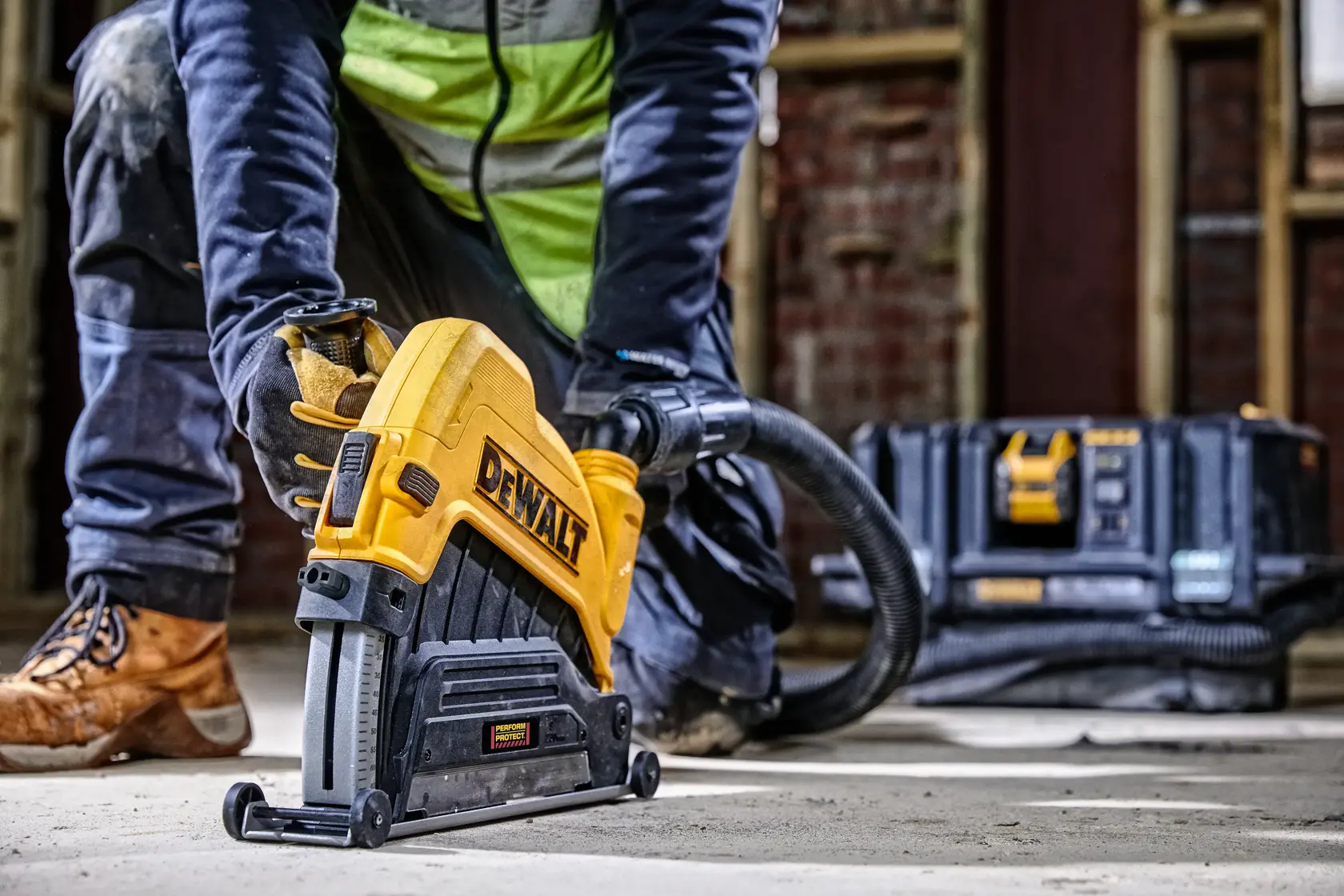 Arbeiter nutzt DEWALT-Werkzeug auf dem Boden; Werkzeugkasten und Schlauch im Hintergrund.