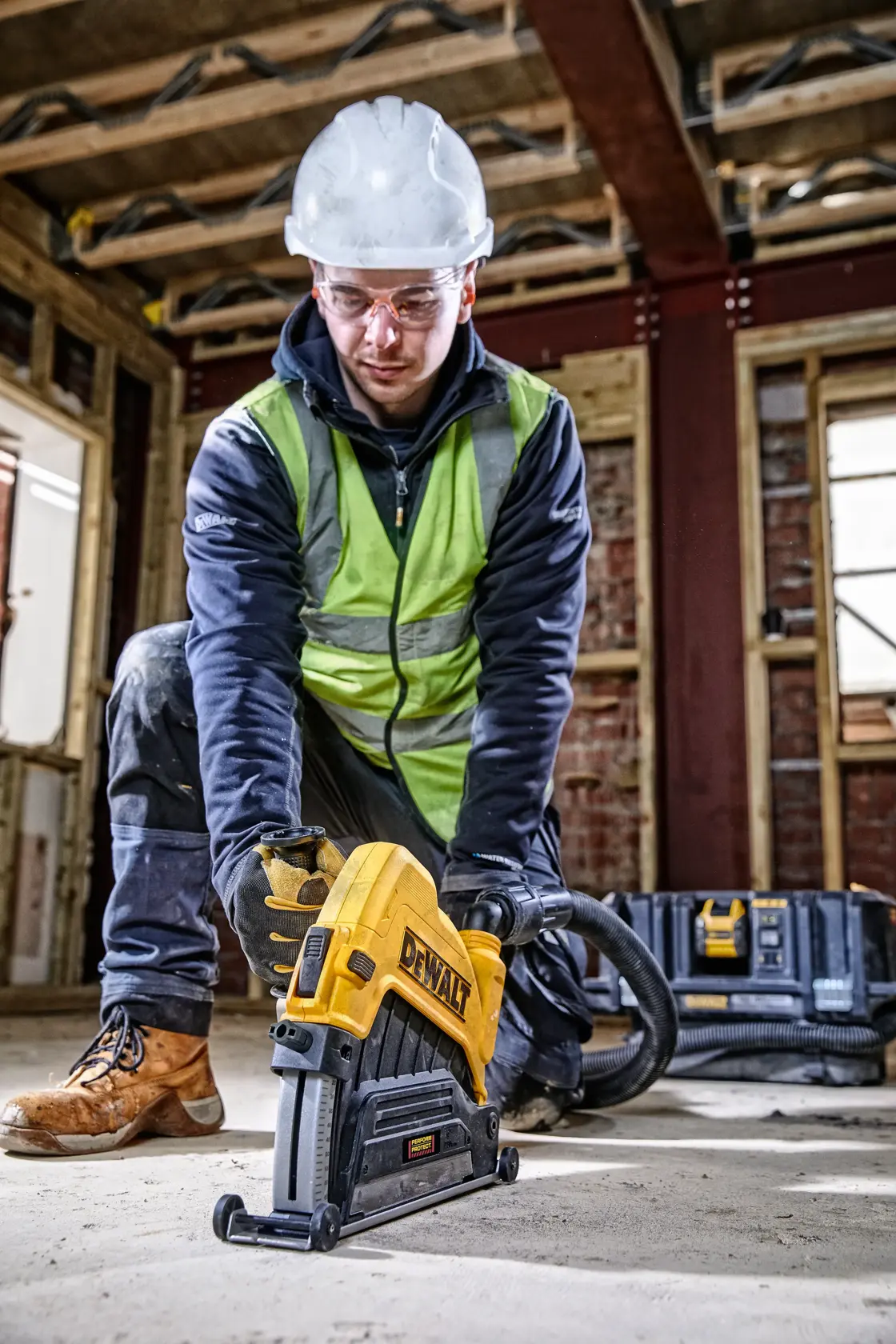 Arbeiter nutzt DEWALT-Werkzeug am Boden der Baustelle mit Schutzausrüstung und Handschuhen.