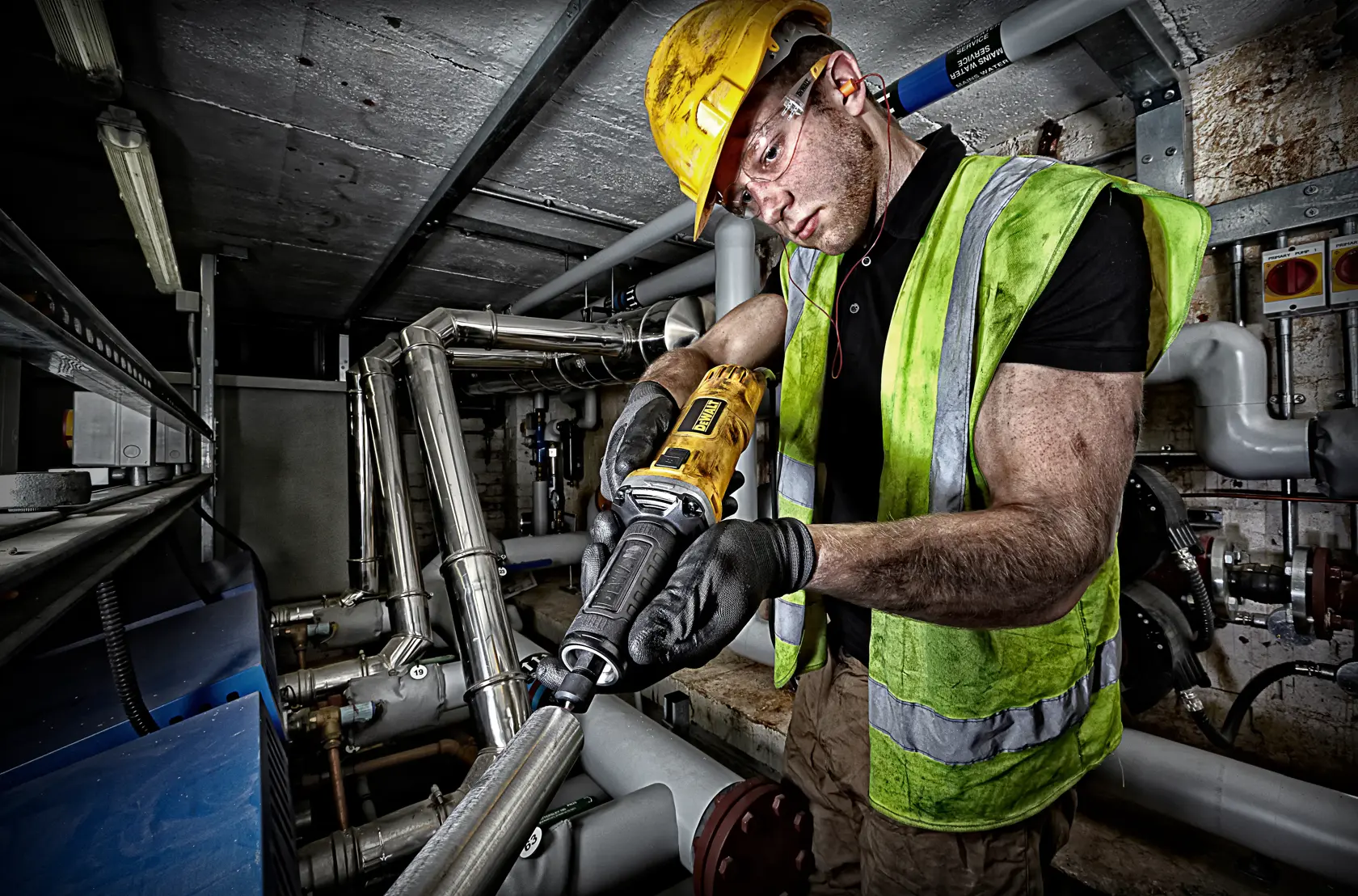 Arbeiter nutzt DEWALT DWE4884 Werkzeug an Metallrohren, trägt Sicherheitsausrüstung und Handschuhe.