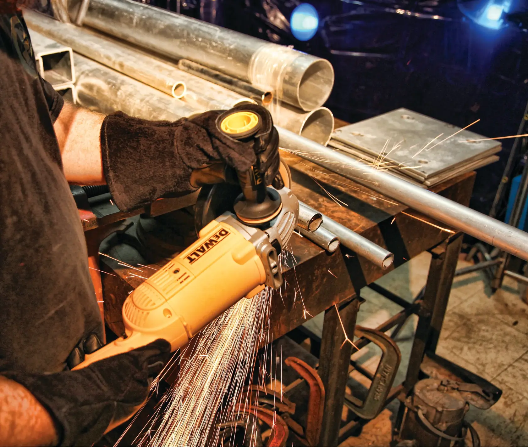 Eine Person mit schwarzen Handschuhen verwendet einen DEWALT-Winkelschleifer, um ein Metallrohr zu schneiden, wobei Funken an einem Werkstatttisch fliegen.
