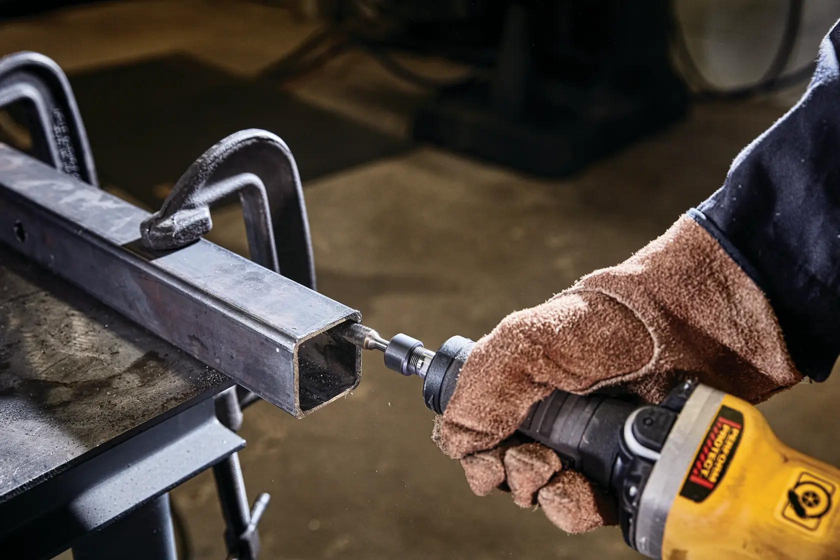 Hand mit Handschuh verwendet DEWALT Werkzeug zum Schleifen von Metall in einem geklemmten Vierkantrohr.