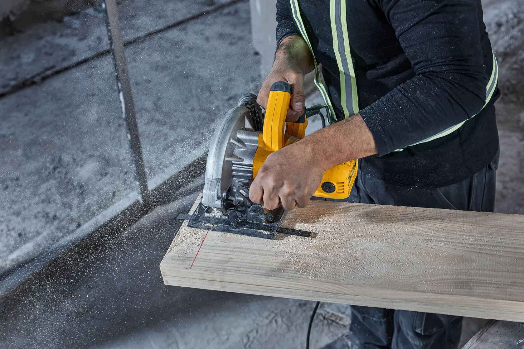 Eine Person verwendet eine gelbe DEWALT-Kreissäge (Modell DWE5615), um ein Holzbrett zu schneiden. Sägemehl und Sicherheitsausrüstung sind sichtbar.
