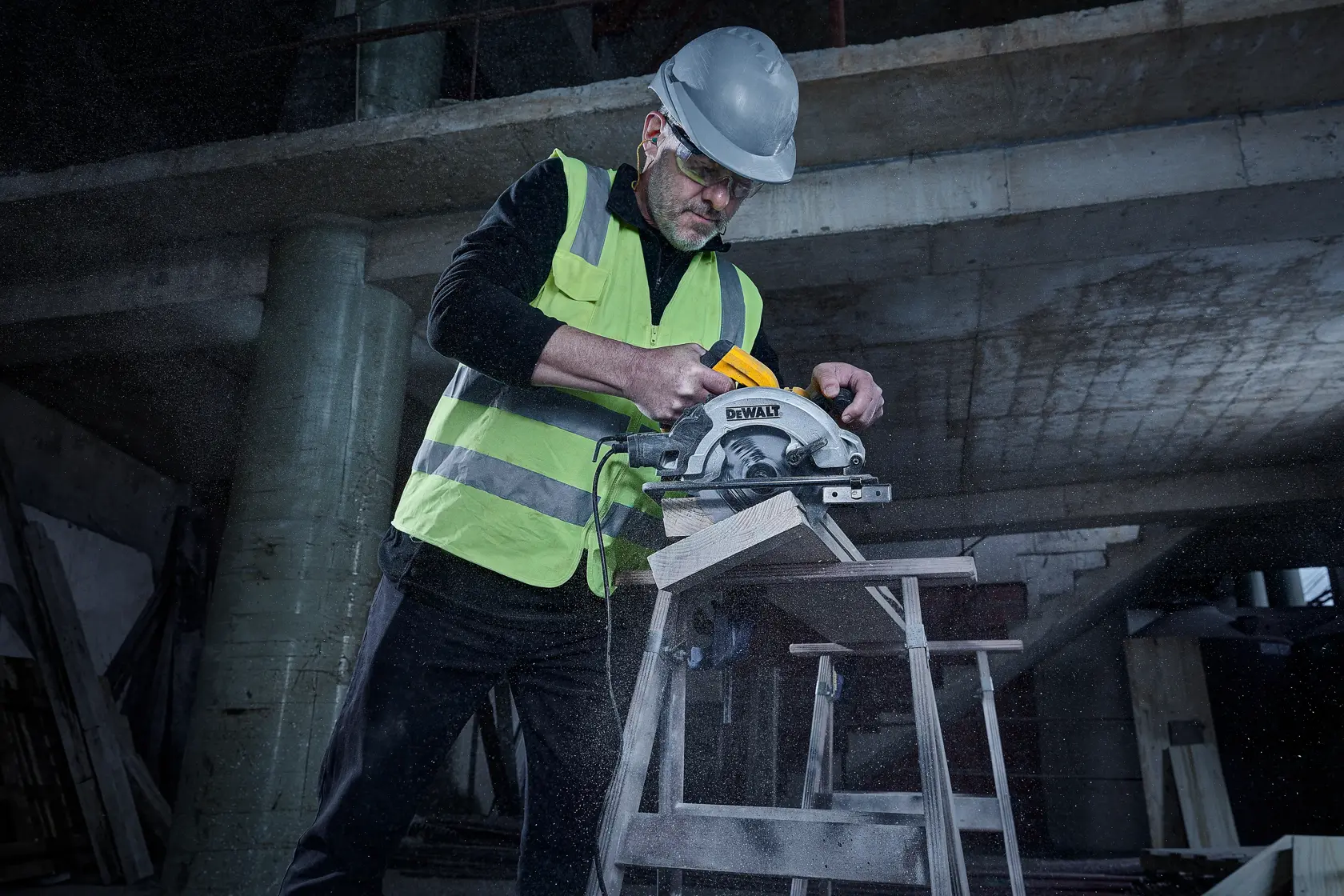 Eine Person mit Sicherheitshelm und reflektierender Weste verwendet eine DEWALT DWE5615 Kreissäge zum Schneiden von Holz auf einer Baustelle. Im Hintergrund ist ein teilweise gebautes Gebäude und verstreute Baumaterialien zu sehen.