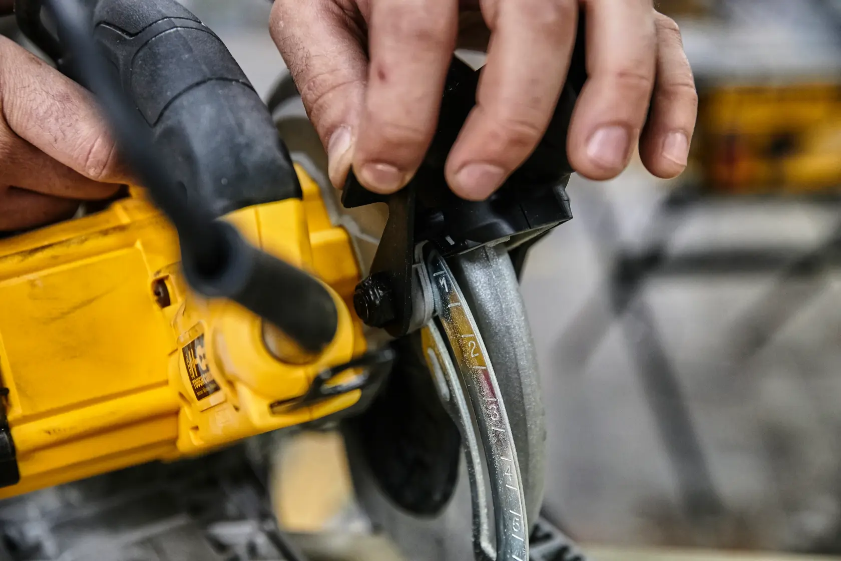 Hand stellt die Tiefeneinstellung einer gelben DEWALT Kreissäge ein.
