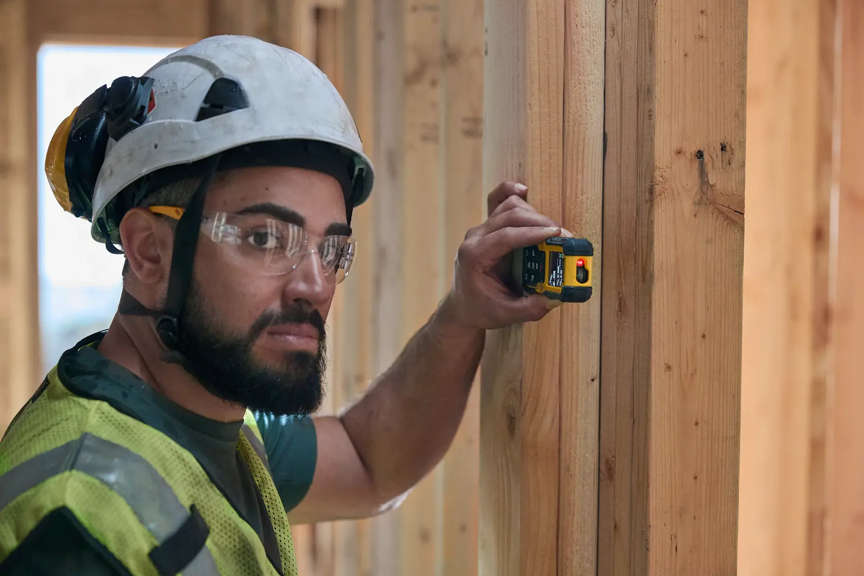 Trabajador usa medidor láser DEWALT en viga de madera en obra de construcción.