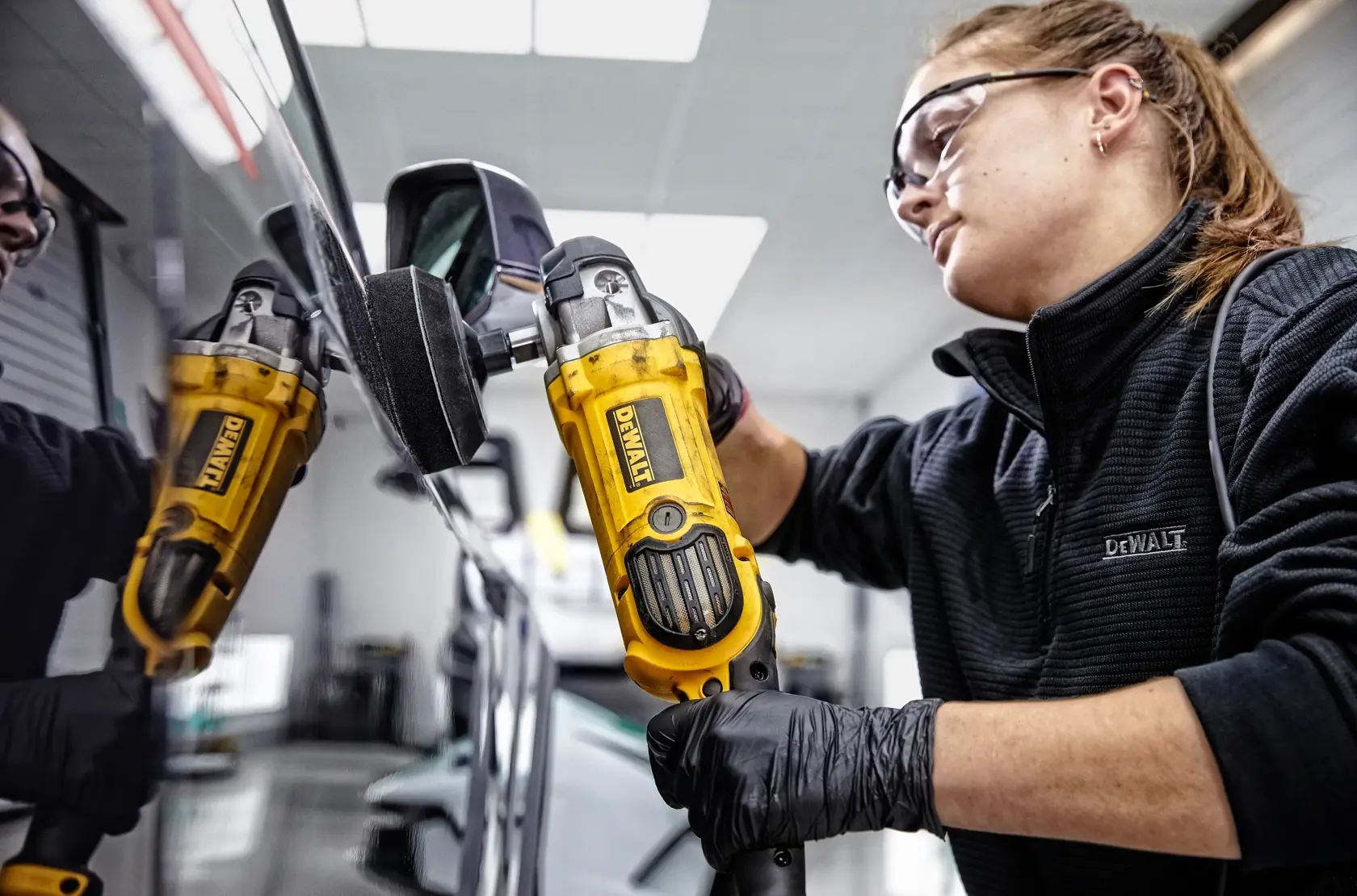 Eine Person poliert die Motorhaube eines roten Sportwagens mit einer DEWALT DWP849X Poliermaschine in einer Garage.