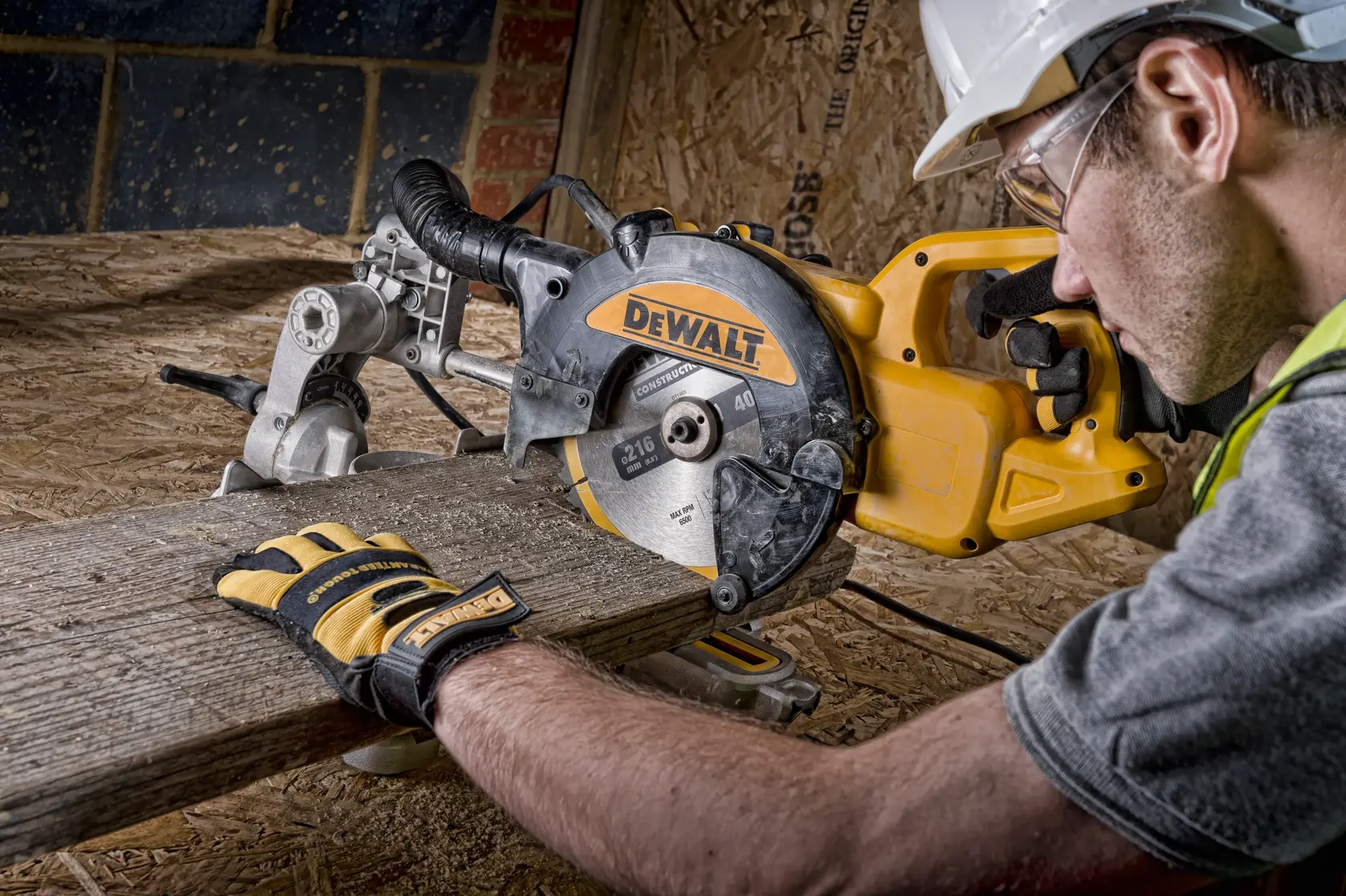 Mit einer DEWALT DWS773 Säge wird Holz geschnitten. Person mit Handschuhen arbeitet auf Baustelle.