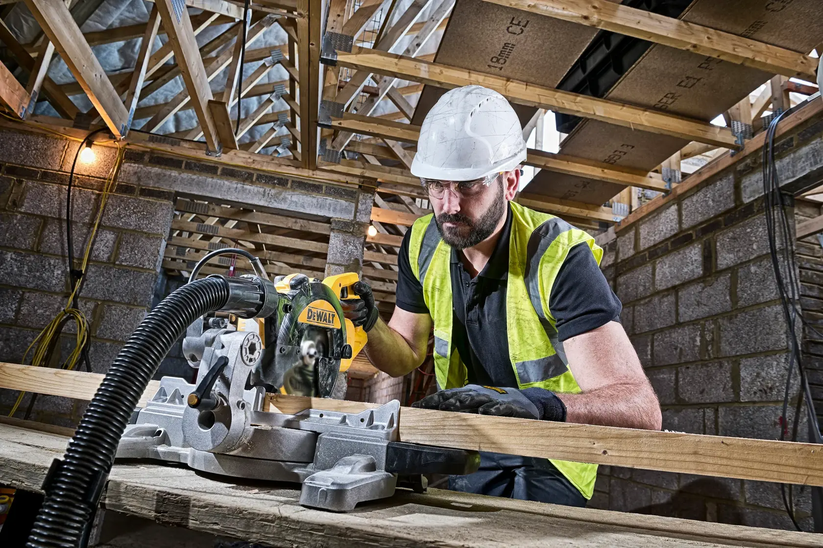 Arbeiter sägt Holz mit DEWALT DWS774 auf Baustelle, trägt Helm und Sicherheitsweste.
