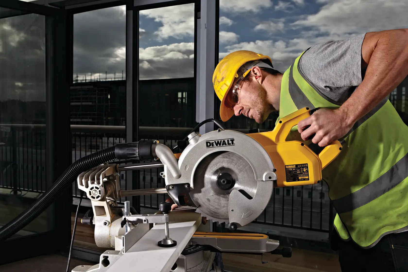 Arbeiter nutzt eine DEWALT DWS778 Säge am Arbeitsplatz, mit Sicherheitskleidung, drinnen an Fenstern.