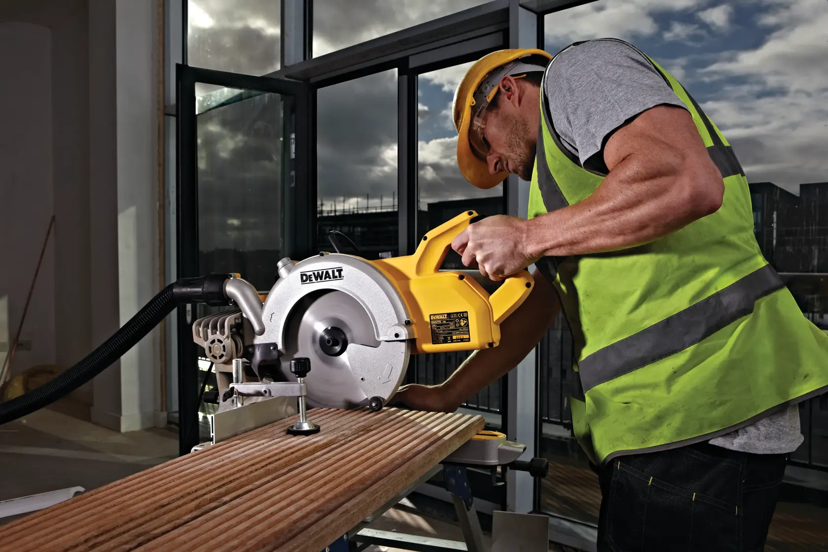 Arbeiter nutzt DEWALT DWS778 Säge zum Holzschneiden drinnen, trägt Schutzweste und Helm.