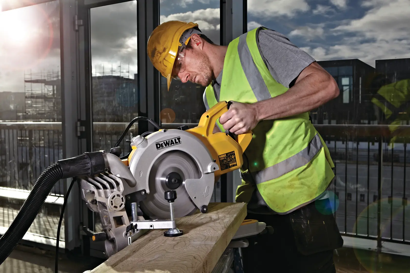 Arbeiter mit Schutzkleidung benutzt DEWALT DWS778 Säge zum Schneiden von Holz, Sonnenlicht durch Fenster sichtbar.