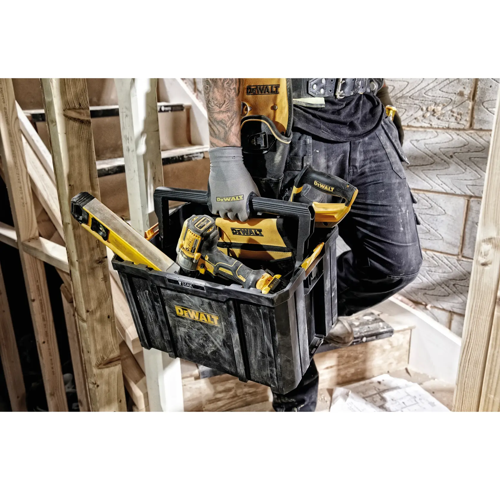 Person hält einen DEWALT Werkzeugkasten mit Werkzeugen auf Baustelle. Ein Bohrer und eine Wasserwaage sind drin.