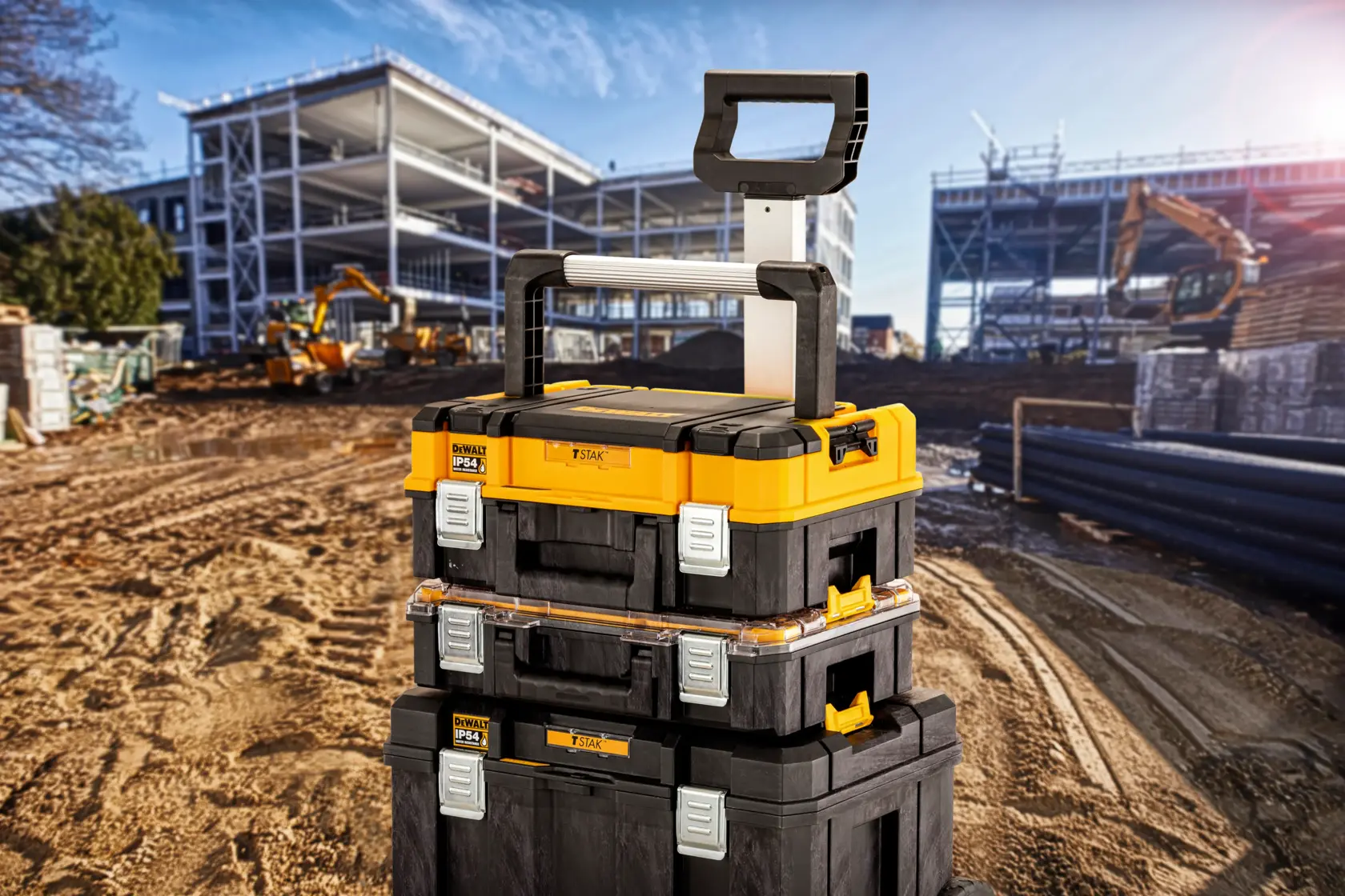 Gestapelte DEWALT Werkzeugkästen mit Griff auf Baustelle, Metallrahmen und Maschinen im Hintergrund sichtbar.