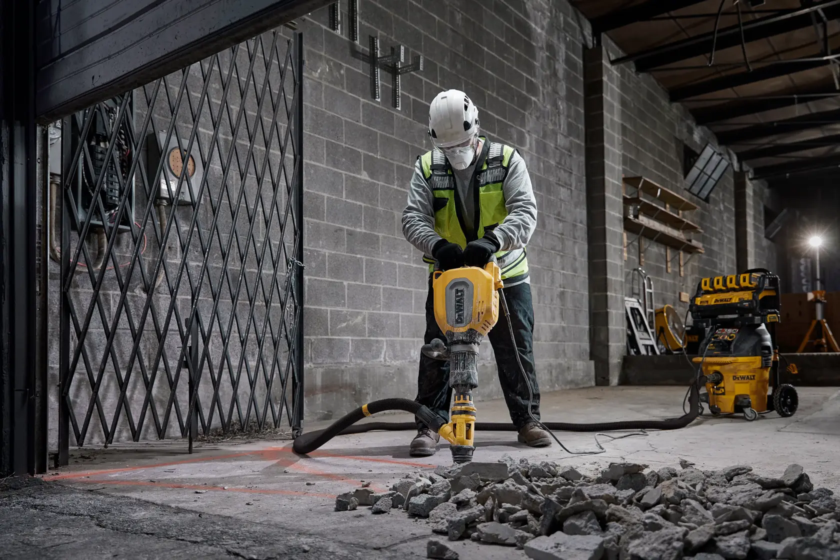 Arbeiter bricht Beton mit DEWALT-Gerät innen. DEWALT-Staubsauger im Hintergrund.