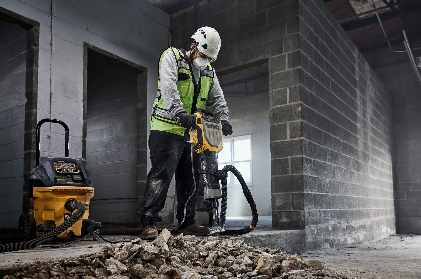 Arbeiter verwendet DEWALT Abbruchhammer und Staubabsauger im Schutt eines Industriebaus.